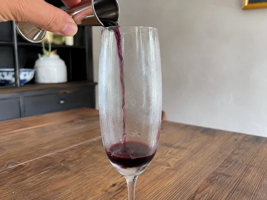 Crème de cassis versée au fond du verre pour préparer un kir breton